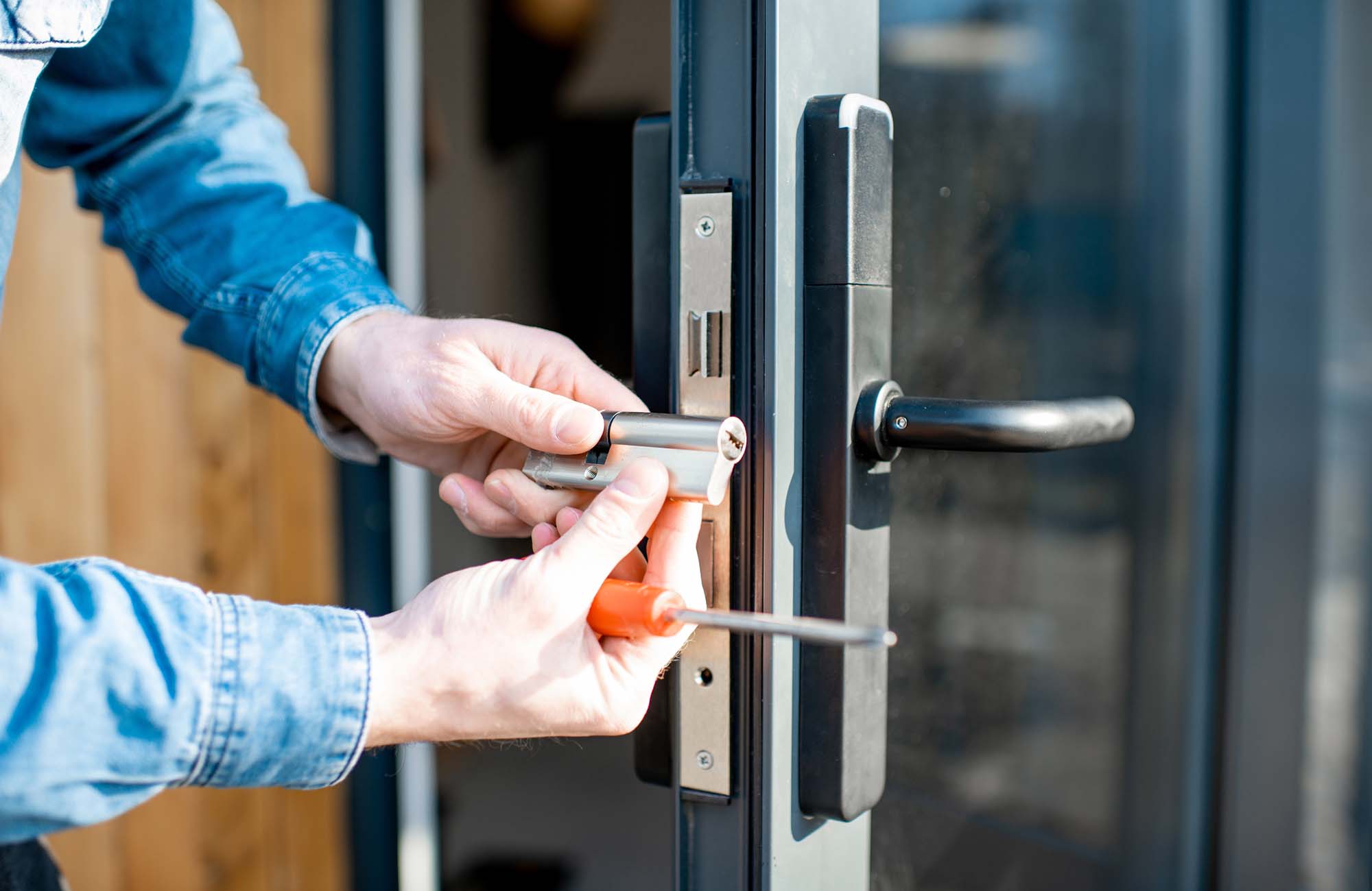 Man changing core of a door lock of the entrance glass door, close-up view with no face in Ashford. Kent