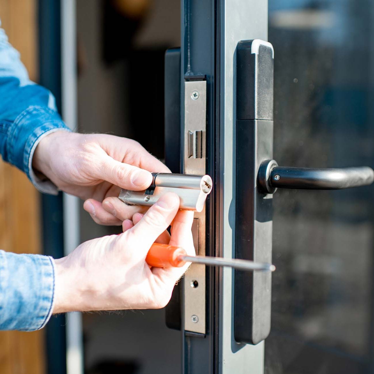 Man changing core of a door lock of the entrance glass door, close-up view with no face in Ashford. Kent